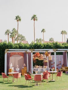 an outdoor wedding reception set up with pink and gold chairs, white table cloths, and palm trees in the background