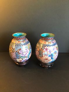 two vases sitting side by side on a black surface with flowers painted on them