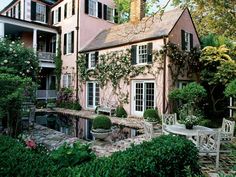 the house is pink with white trim and windows on both sides, surrounded by greenery