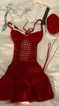 a crocheted red dress laying on top of a bed next to a ball of yarn