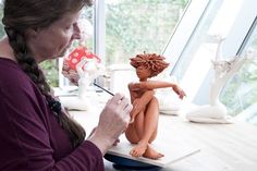 a woman sitting at a table writing on a piece of paper next to a small figurine