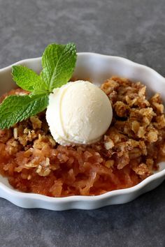 a bowl filled with fruit and ice cream sitting on top of a gray table next to a green leaf