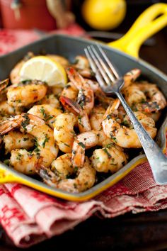 a skillet filled with shrimp and garnished with lemon wedges