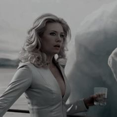 a woman standing next to a polar bear holding a drink in her hand and looking at the camera