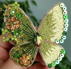 a hand holding a green and yellow butterfly brooch with beads on it's wings