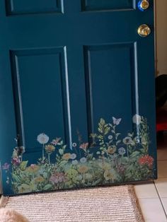 a cat sitting on the floor in front of a blue door with flowers painted on it