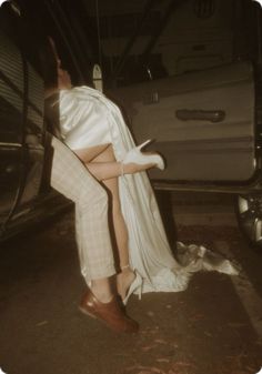 a man sitting on the back of a car next to a woman in high heels