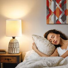 a woman laying in bed with her eyes closed while holding a pillow and looking at the camera