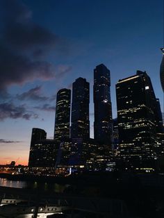 the city skyline is lit up at night, with skyscrapers in the foreground