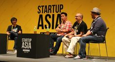 four men sitting on stage talking to each other in front of a yellow sign that says start up asia