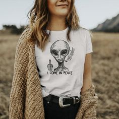 a woman wearing a t - shirt that says i come in peace with an alien on it