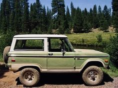 a green and white truck parked on top of a dirt road next to a forest