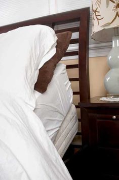 a bed with white sheets and pillows next to a night stand on a nightstand in a bedroom