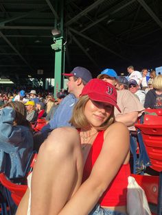 a woman sitting in the stands at a baseball game wearing a red hat and blue jeans