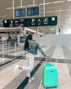 a woman with her arms in the air while pulling a green suitcase through an airport