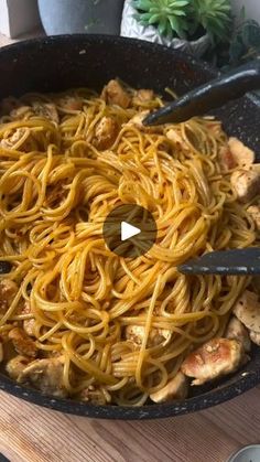 a skillet filled with pasta and chicken on top of a wooden table