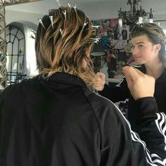 a woman is brushing her hair in front of a mirror while another person looks on