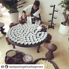 a woman is arranging cups on a table in a room filled with potted plants