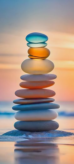 a stack of rocks sitting on top of a beach next to the ocean at sunset