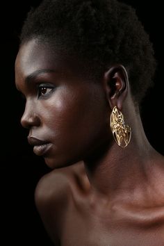 a woman with dark skin wearing gold earrings