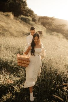 a man and woman are walking through the grass with baskets in their hands while holding each other's arms