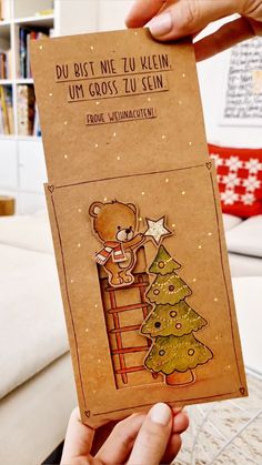 someone holding up a christmas card with a teddy bear on the top and a tree on the bottom