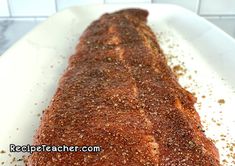 a large piece of meat sitting on top of a white plate next to some seasoning