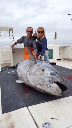 a man and woman standing next to a large fish on the back of a boat