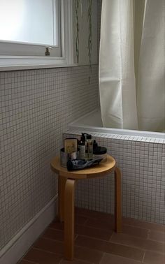 a small wooden table sitting in front of a window next to a bathtub filled with personal care items