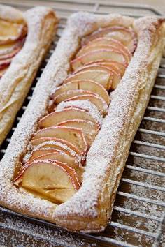 two pastries sitting on top of a cooling rack covered in powdered sugar and apple slices