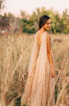 a woman standing in tall grass with her back to the camera and wearing a dress