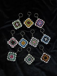 six key chains with different colors and designs on black fabric, one is made out of glass beads