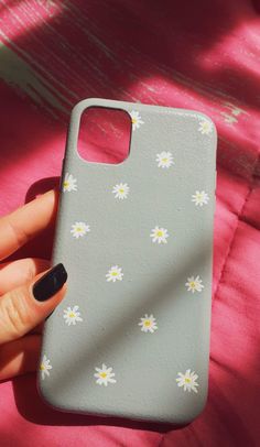 a woman's hand holding up a phone case with daisies on the back