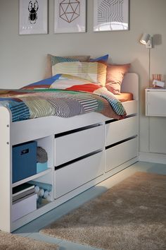 a white bed with drawers underneath it and pictures above the headboard on the wall