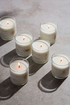 six white candles sitting on top of a cement floor next to each other with one lit candle in the middle