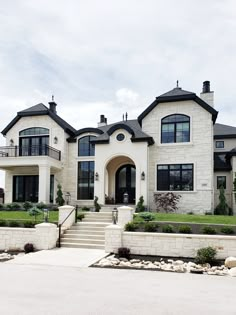 a large white house with lots of windows and landscaping on the front lawn, along with steps leading up to it