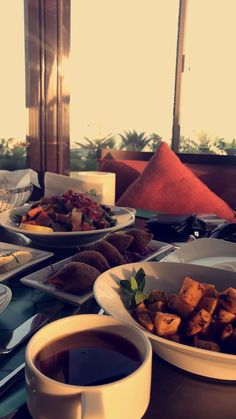 a table filled with plates and bowls of food next to a cup of coffee on a saucer