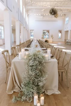 a long table with candles and flowers on it in the middle of a large room