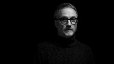 black and white photo of man with glasses looking at the camera in dark room,