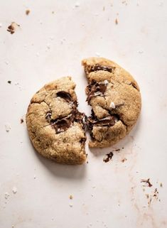 two chocolate chip cookies on a white surface with one broken in half and the other partially eaten