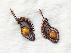 two pairs of earrings on top of a white furnishing area, one has an orange bead and the other is brown