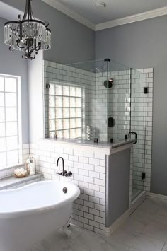 a white bath tub sitting under a chandelier next to a window in a bathroom