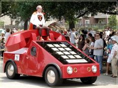 a man sitting on top of a red car in the middle of a street filled with people