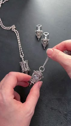 a person holding onto some silver jewelry on a black table with other items in the background