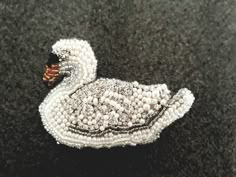 a beaded swan brooch sitting on top of a black carpeted floor next to a white wall