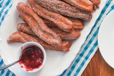 powdered sugar churros on a white plate next to a bowl of jelly