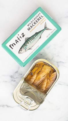 an open can of mackerel next to a box of mackerel on a marble surface