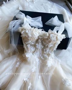 a wedding dress with flowers on it is laying on the floor next to a black box