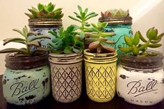 four painted mason jars with succulents in them sitting on a table next to each other