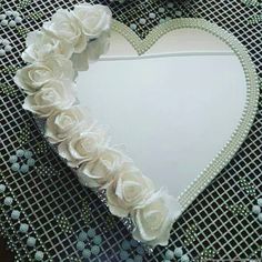 a white heart shaped mirror with flowers on the edge and beaded border around it